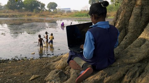 District Katni, Madhya Pradesh, India - January 04, 2021: An asian village poor government school girl kid learning about laptop on village background on water pond view video footage.