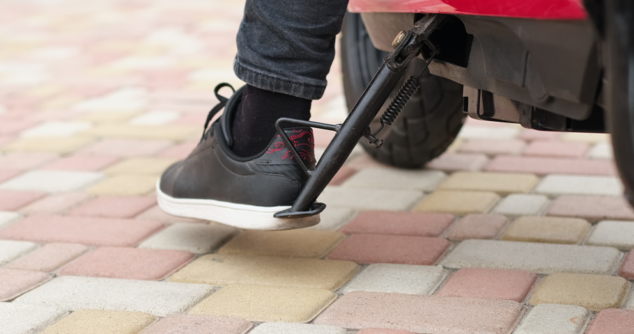 A person raises the parking step of the moped with his foot to start driving. Parking a moped on the street. Close-up from below.