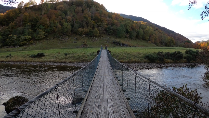 POV walking on squeaky wobbly wooden and metal bridge across river in Glen Lyon, Scottish Highlands