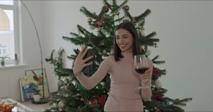 Camera view of young caucasian female using smart phone video call talking with friends, Christmas tree decorated with ornament in living room at home. Social distancing, New Year holiday festival.