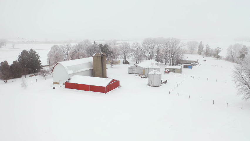 Establishing shot of Midwestern countryside in winter season.  Aerial view of farm, agricultural fields. Cold misty weather with snow and frost