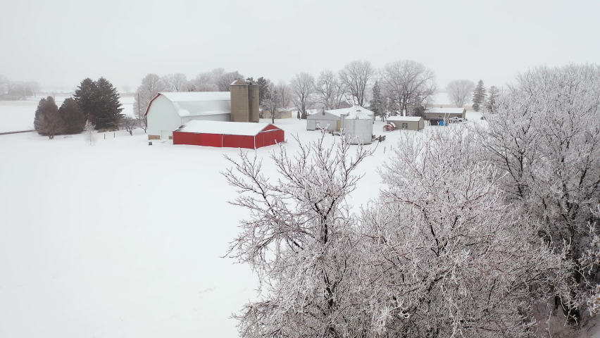 Establishing shot of Midwestern countryside in winter season.  Aerial view of farm, agricultural fields. Cold misty weather with snow and frost