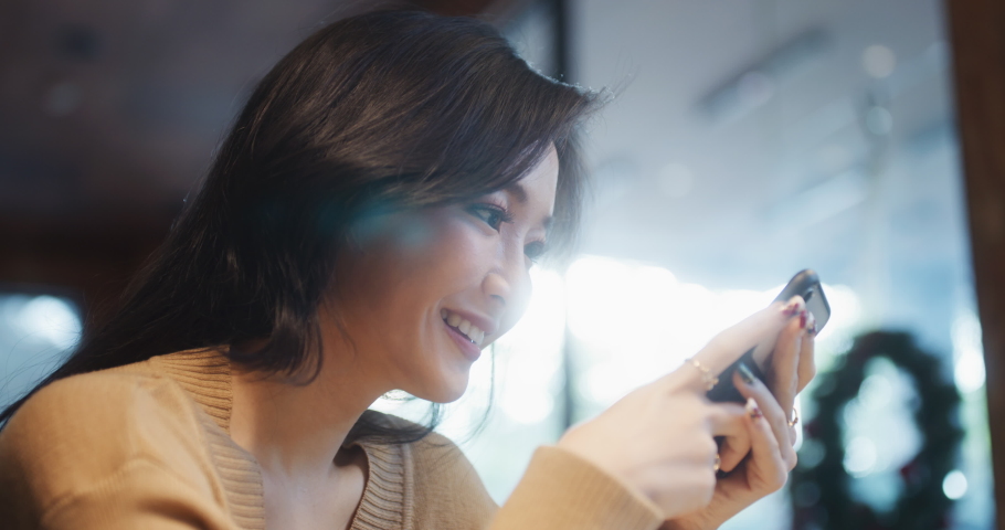 Beautiful young Asian woman using smartphone in coffee shop, happy smiling. People lifestyle, internet communication technology, or online shopping concept. Handheld slow motion Royalty-Free Stock Footage #1064995249