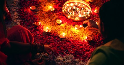 Slow-motion of Indian couple in pink green decorating house for Diwali- traditional festival with colorful orange marigold red rose flower petals, oil lamps, candles and brass bowl night outdoors