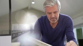 Attractive senior man with eyeglasses relaxing at home reading newspaper - Powered by Shutterstock - Get 15% off with code: PIKWIZARD15
