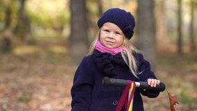 4k video portrait of cute caucasian pretty blond calm baby girl standing alone in beautiful autumn park outdoor.