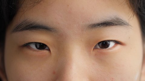 Close up of young Asian woman opening her beautiful eyes and looking at camera. Portrait of Chinese girl with pretty face, soft features, healthy skin, and dark brown or black eyes. Slow motion, 4K.