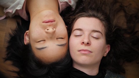 Two beautiful young women lying on floor waking up and opening eyes. Portrait of Asian and Caucasian girls side-by-side. Concept of interracial friendship or female mixed-race homosexual couple. 4K. 庫存影片