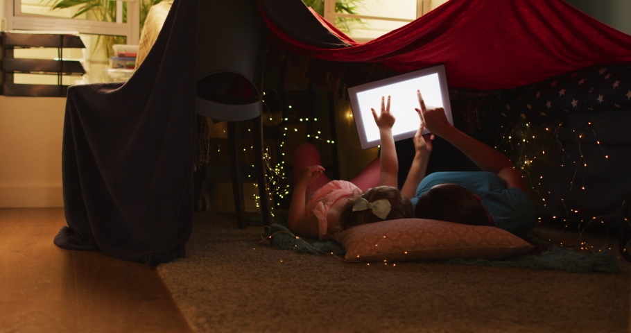 Caucasian mother and daughter having fun using digital tablet. lying in bedroom fort together. enjoying quality time at home during coronavirus covid 19 pandemic lockdown.