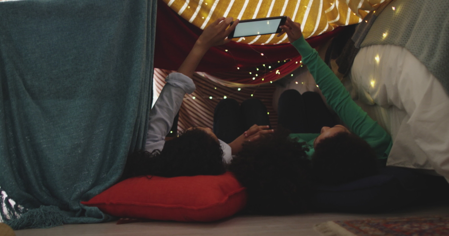 Mixed race lesbian couple and daughter using tablet lying in bedroom camp. self isolation quality family time at home together during coronavirus covid 19 pandemic.