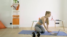 woman in sportswear on a mat at home looking for sports tutorials using a laptop
