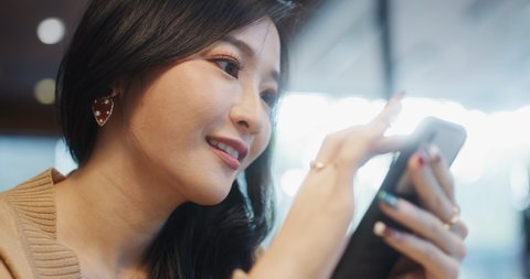 Beautiful young Asian woman using smartphone in coffee shop, happy smiling. People lifestyle, internet communication technology, or online shopping concept. Handheld slow motion. Shot on RED Komodo 6K