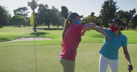 Two caucasian women playing golf wearing face masks greeting each other with elbows. golf cart and clubs in background. golf sports hobby healthy lifestyle hygiene during covid coronavirus pandemic.