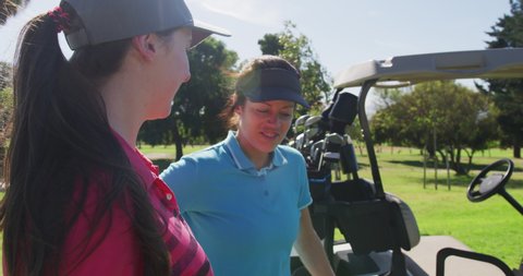 Two caucasian women playing golf going into a golf cart. golf clubs in background. golf sports hobby healthy lifestyle.