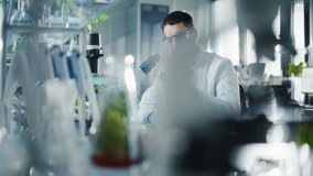 Handsome Male Scientist in Safety Glasses Analyzing a Lab-Grown Tomato Through an Advanced Microscope. Microbiologist Working on Molecule Samples in Modern Laboratory with Technological Equipment. - Powered by Shutterstock - Get 15% off with code: PIKWIZARD15