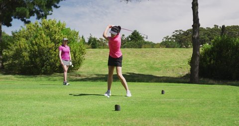 Two caucasian women playing golf one taking shot from bunker. golf cart and clubs in background. golf sports hobby healthy lifestyle.