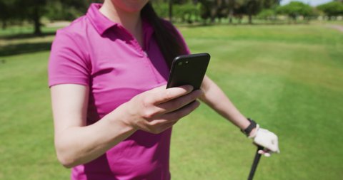Caucasian woman playing golf using a smartphone. golf cart and clubs in background. golf sports hobby healthy lifestyle.