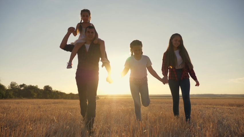 Cute happy family walks park in evening at sunset.Parents, children,dads,mother,daughter walk holding hands across field.Young happy family enjoy socializing together in park.Children, loving parents. Royalty-Free Stock Footage #1065024883