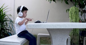 Asian little boy using laptop and headphones in the home garden, E-learning online education and home schooling concept