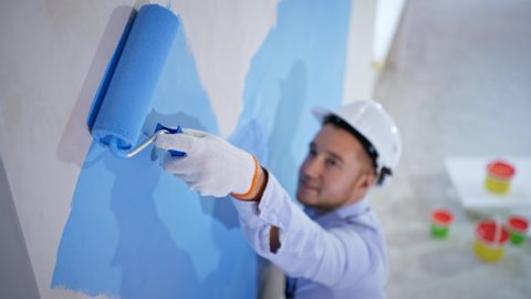 apartment redecoration and home construction while renovating and improving, young painter performs finishing work uses roller to paint walls, close-up