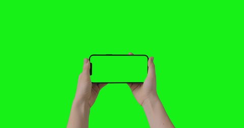 iPhone 12 Pro Max isolated on chroma key. Woman hands hold phone with a green screen in a horizontal orientation landscape mode. Mockup for compositing. 2021 - USA, NY