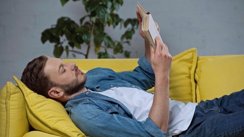 concentrated man reading book while lying on sofa