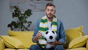 cheerful man sitting on sofa and playing with soccer ball