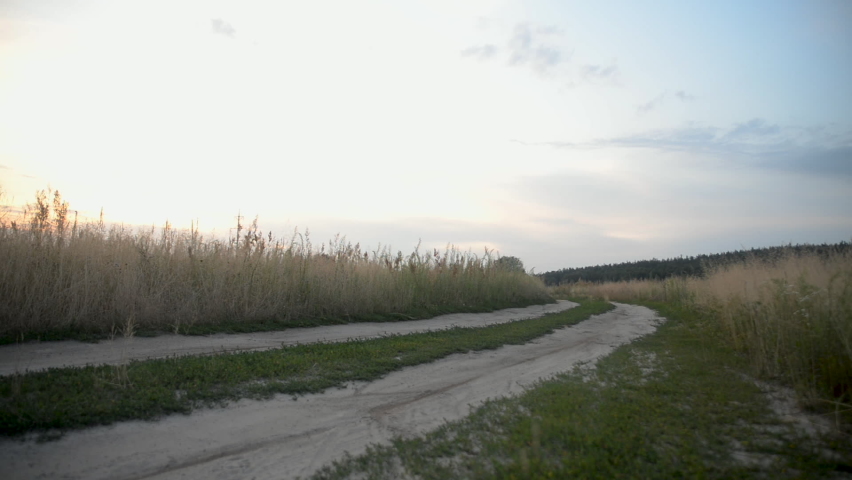 Cyclist rides a bicycle dirt trail in a field at sunset.