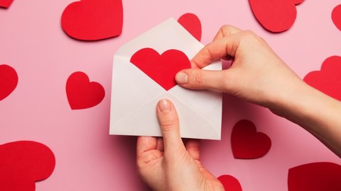 Hands open a delivered envelope letter with a valentine in the shape of a red heart for the holiday valentine's day. Declaration of love, relationship concept.