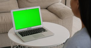 Woman video chatting using laptop with green chroma screen