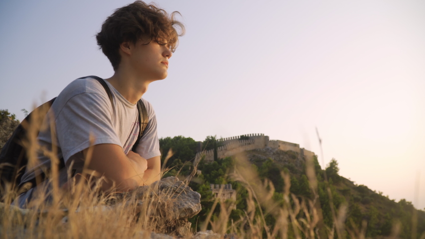Medium shot of a young man looking at a view at sunset, Fortress and mountains in the background, Alanya, Turkey