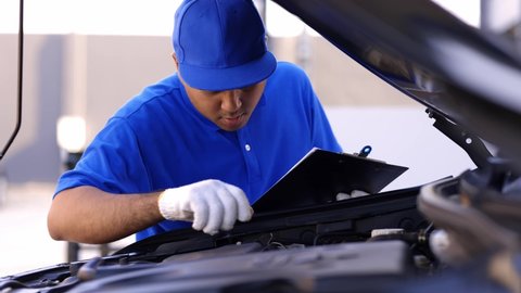 A young Asian auto mechanic opens the bonnet. To check for engine damage And perform professional maintenance. He wearing blue uniform.