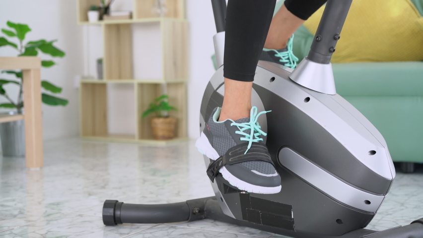 Close up of fitness woman in sport clothing exercising legs on static bike workout at home