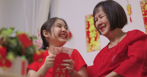 Happy Senior Asian Woman Giving Her Granddaughter A Lucky Red Envelope for Chinese New Year Gift. (Foreign Texts Mean Congratulations, Wealth, Good luck, Good Fortune, Spring)