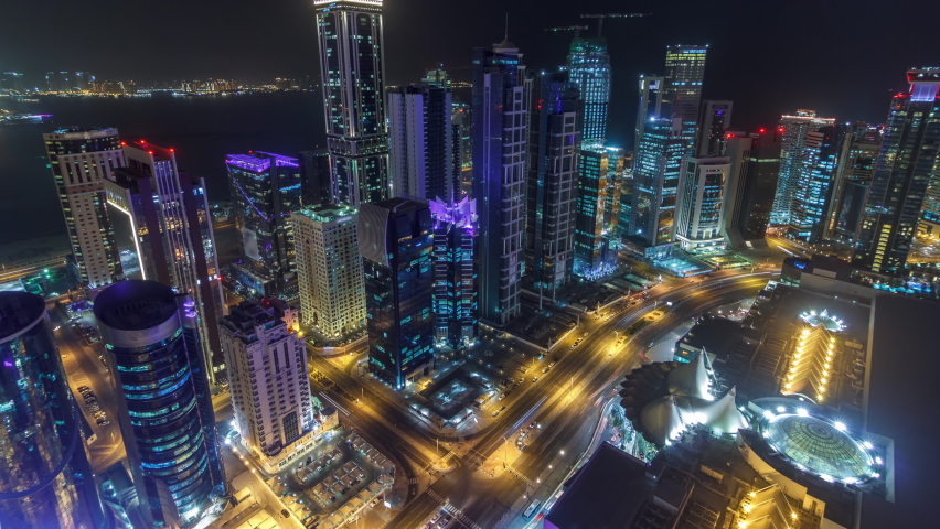 The skyline of the West Bay area from top in Doha timelapse, Qatar. Illuminated modern skyscrapers aerial view from rooftop at night. Traffic on the road