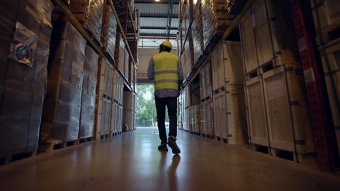 Rear view of Professional male warehouse worker wearing hard hats walking and checks inventory stock on the shelf in fulfillment center. eCommerce business and freight transportation logistic concept.