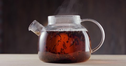 In a glass teapot filled with boiling water and large leaf tea, brewed black tea leaves slowly swirl. Dark brown background, slow motion 150 fps, Blackmagic Ursa Pro G2. 