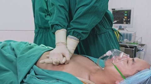 Group of doctors in Hospital Operating Room. Asian professional surgeons and nurses team making cpr and use defibrillator electric device to shock heart on intensive care patient during operation.