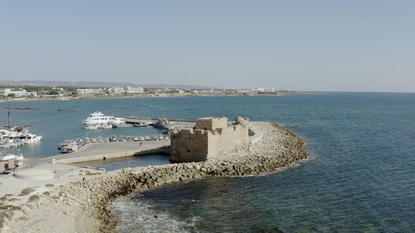 
Drone flying over the old historic fort that stands on the shores of the Mediterranean Sea against the shoreline of which the waves crash. Aerial view Paphos Cyprus.
