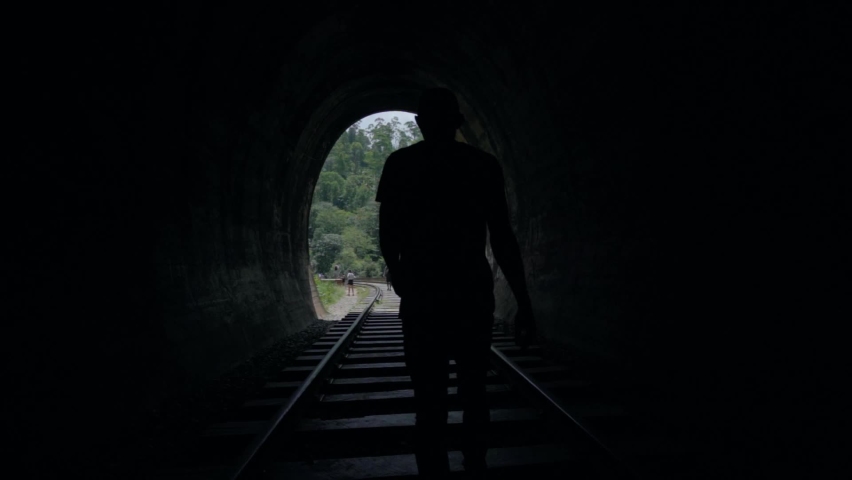 Slow Motion man walking in railway Tunnel to Light