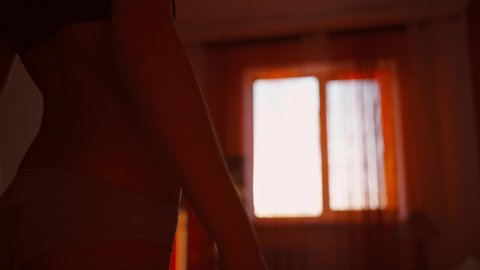 silhouette of sensual unrecognizable woman in lingerie in bedroom against window with sunset sunlight. brurred footage