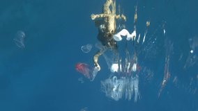 VERTICAL VIDEO: Woman collects plastic garbage underwater clean up of a dirty discarded plastic waste floating in the sea. Snorkeler catches plastic trash from water. Plastic pollution of the Ocean.
