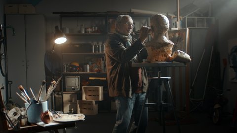 WIDE Portrait of senior adult middle eastern male sculptor working on a bust project in his home garage workshop. Retirement hobby concept. Shot with 2x anamorphic lens