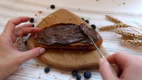 Spread chocolate paste on a piece of fresh bread. Carbohydrates, hearty breakfast, peanut butter sandwich making concept