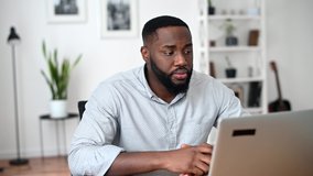 An African American guy in smart casual shirt has meeting online, video call on the laptop indoor, biracial man listens carefully and nods his head in agreement