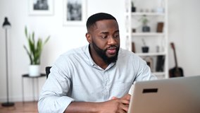 An African American young man waving into webcam and talking online, video call, virtual conference. Positive multiracial employee is greeting in the online meeting on the laptop