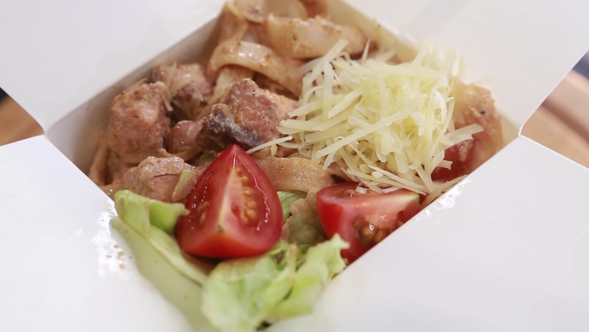 pasta-fituccine with cheese, meat or shrimps, cherry tomatoes with herbs and egg yolk in a takeaway box on a turntable
