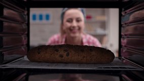 Pretty woman with blonde hair takes out delicious, rich grain and olive bread from the oven. Shooting from inside the oven. Slow motion video.