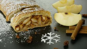 Puff pastry with apple filling. Apple strudel with cinnamon, raisins, cloves and powdered sugar snowflake. Rustic dessert with ingredients. Central european cuisine. 4k video, spinning table.
