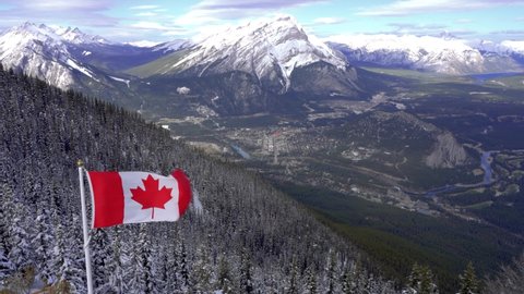 Close-up National Flag of Canada with Town of Banff, Cascade Mountain and surrounding snow-covered Canadian Rocky Mountains in winter. Banff National Park, Alberta, Canada.